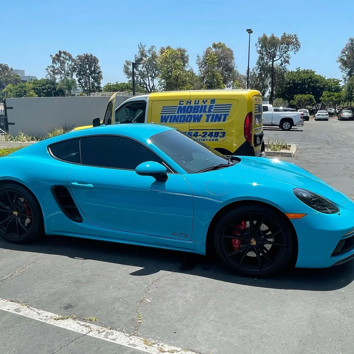 Blue Porsche 718 Cayman GTS with freshly tinted windows beside the Chuy's Mobile Window Tint service van